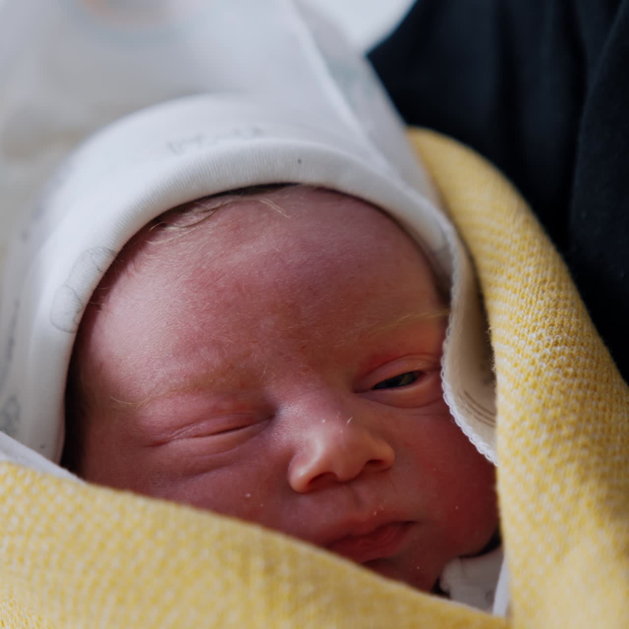 Adorable face of a few minutes old baby. Little newborn covered in blankets in dad's hands. Close up