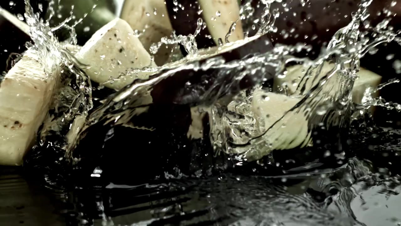 Melanzane fresche tagliate a pezzi che si tuffano nell'acqua al rallentatore