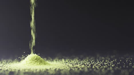 video of close up of green sand grains pouring into heap and copy space on black background