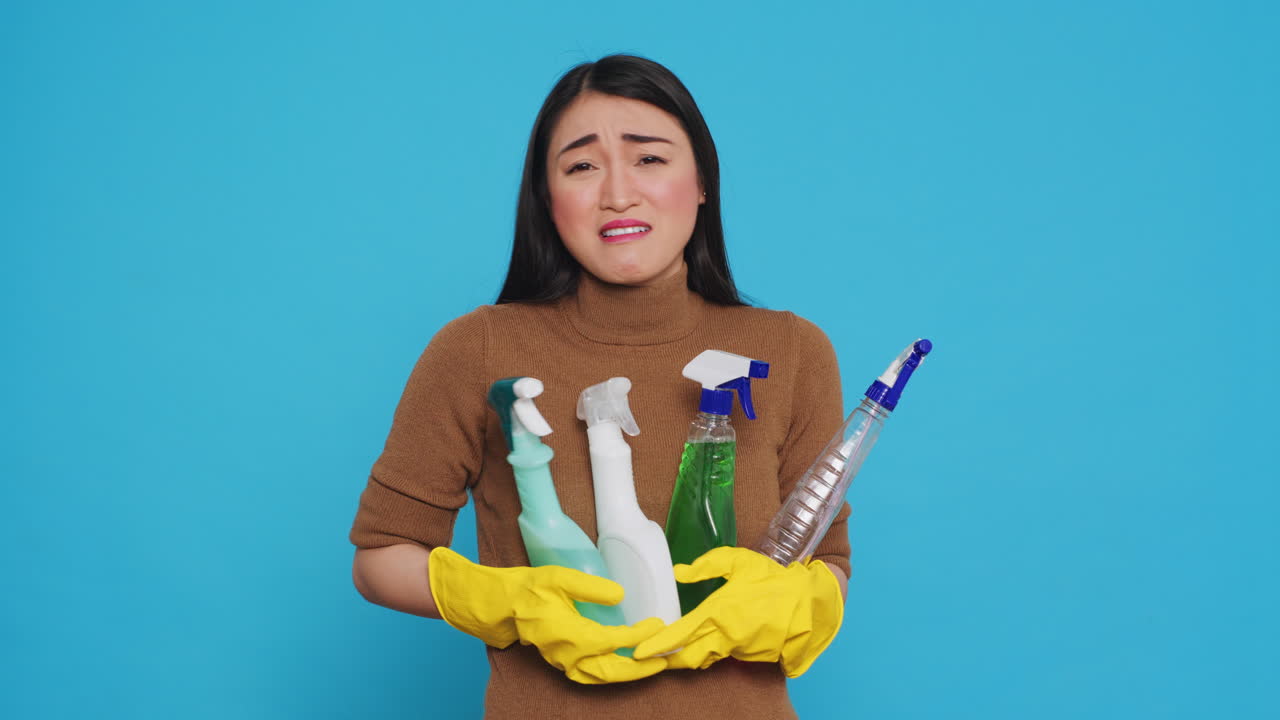 Overwhelmed tired housekeeper wearing gloves while holding multiple sanitary cleanliness products