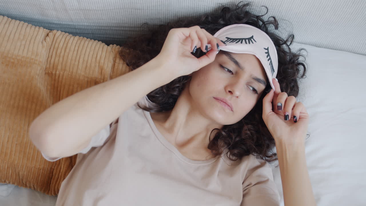 수면 마스크 를 착용 한 여자 가 침대 에서 잠을 자고 있다