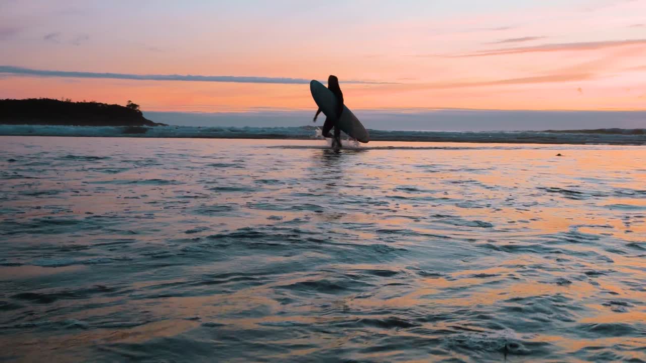 un surfista saliendo del agua al atardecer en tofino, columbia británica