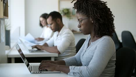 side view of focused african american worker typing on laptop.