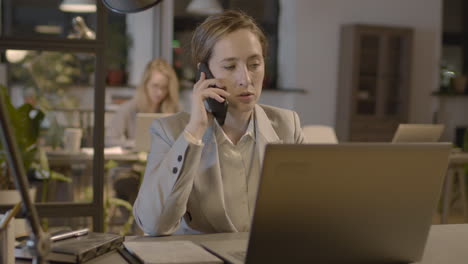 mujer de negocios hablando por teléfono móvil mientras trabaja en una computadora portátil en la oficina