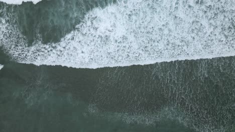 foamy ocean waves rolling towards coastline, top down view