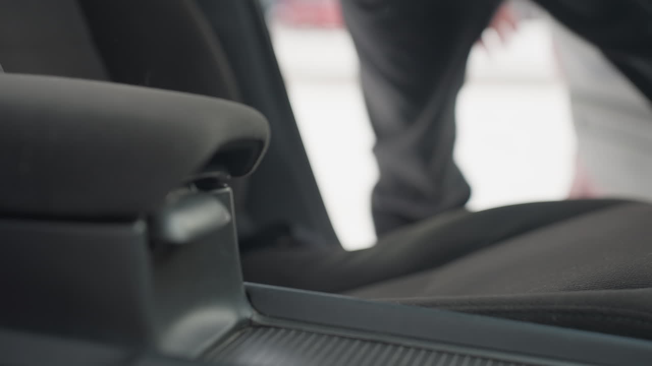close up interior view showing person stepping out of parked car and shutting door with winter snow visible outside, green jacket and dark trousers suggesting cold weather conditions