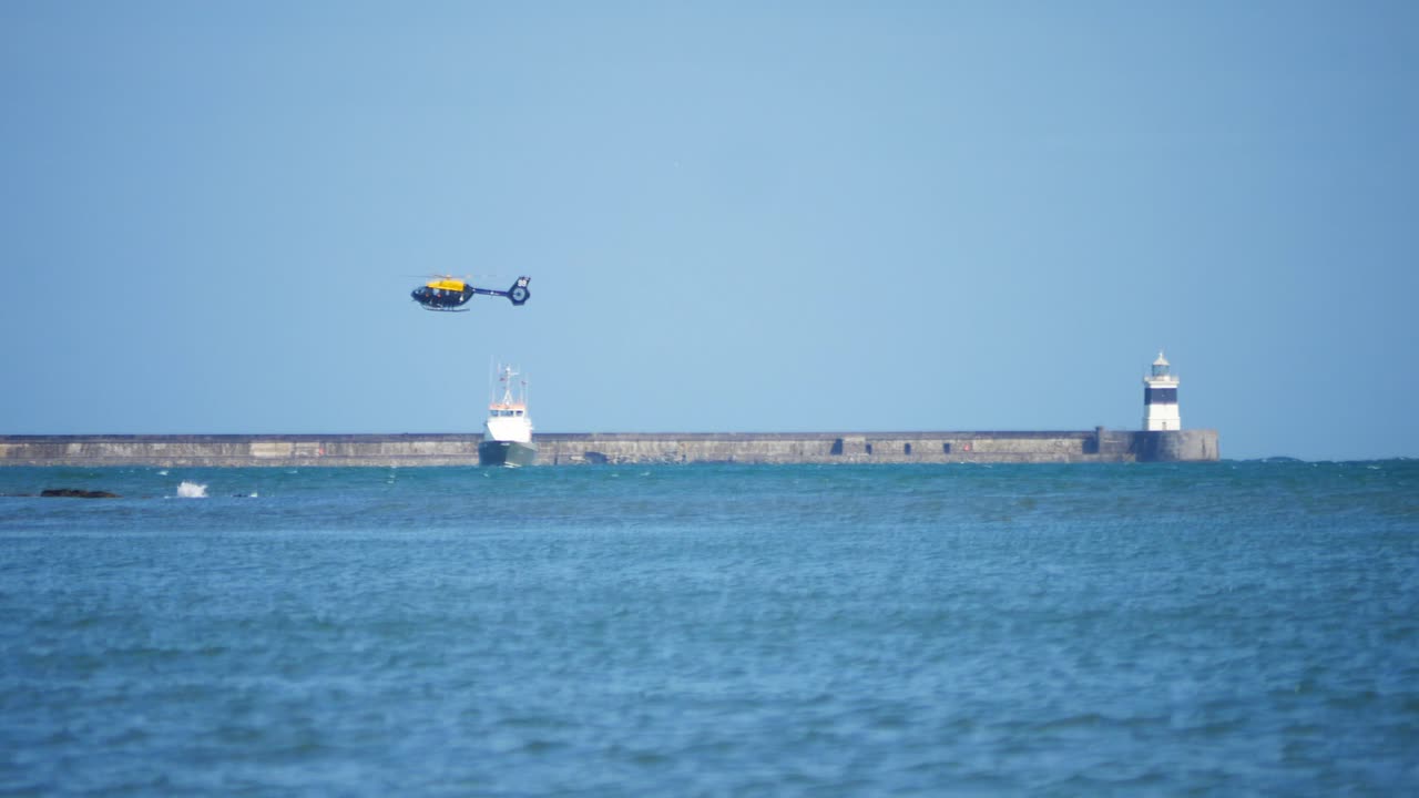 Coast guard helicopter rescue winch training with trawler boat at Holyhead breakwater lighthouse