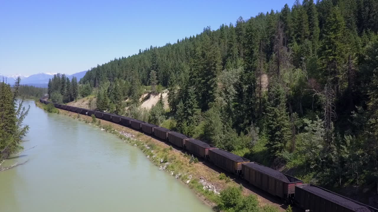 la antena sigue al tren que transporta carbón junto al río bow en las montañas rocosas canadienses