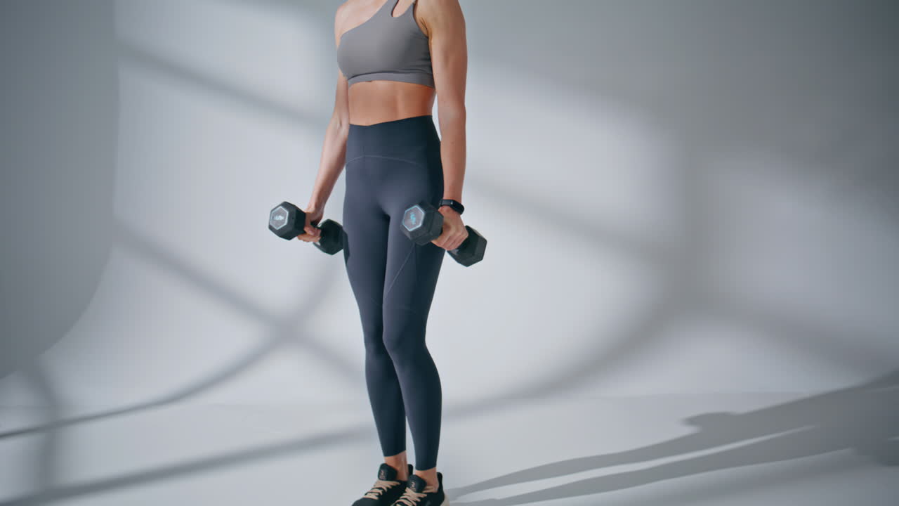 スポーツトレーナーがスタジオでダンベルスクワットをしている様子。筋力トレーニングをする強い女性。