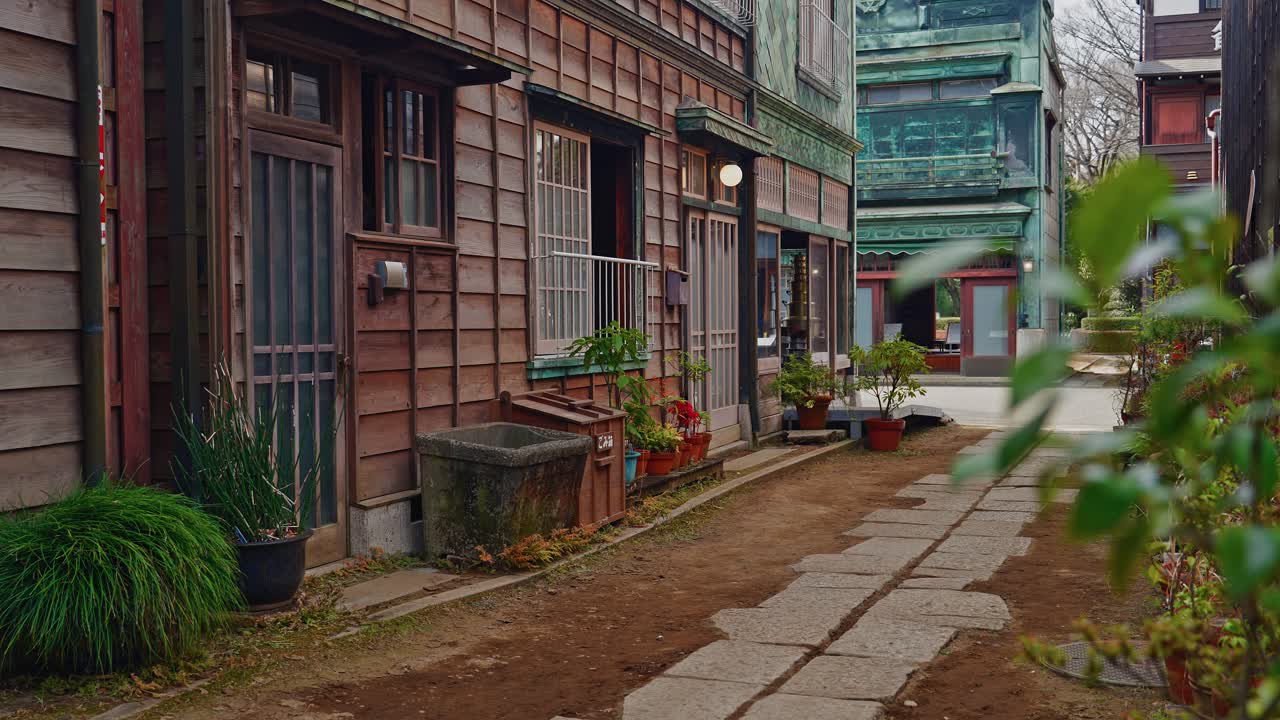 A nostalgic view of a narrow Japanese alley featuring vintage wooden architecture, potted plants, and a traditional stone walkway under soft daylight