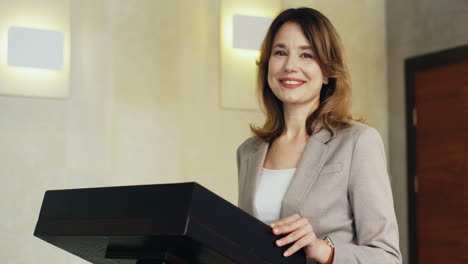 close-up view young caucasian businesswoman in formal clothes on a podium looking at the camera and smiling in a meeting room