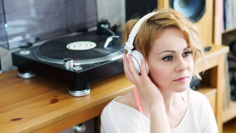 woman sits next to the turntable and listens to music