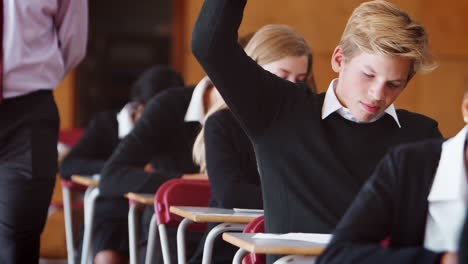 teenage student sitting examination asking teacher question