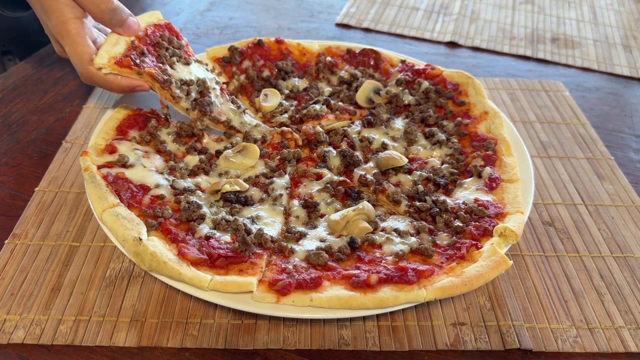 Mano che prende una fetta di deliziosa pizza con carne macinata e funghi