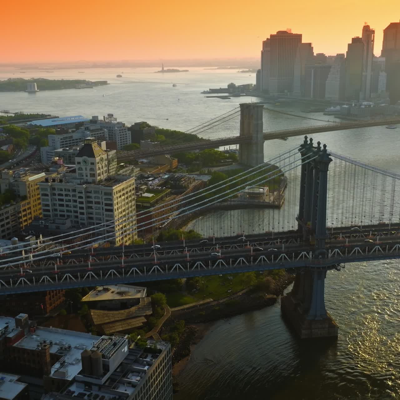 Manhattan and Brooklyn Bridges over East River. Silhouettes of New York skyscrapers at the backdrop of orange skies