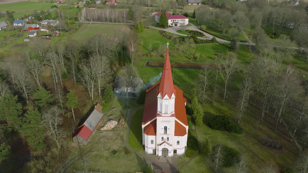 Vista aerea di una chiesa bianca con tetto rosso in una soleggiata giornata primaverile, ripresa orbitale con drone grandangolare.