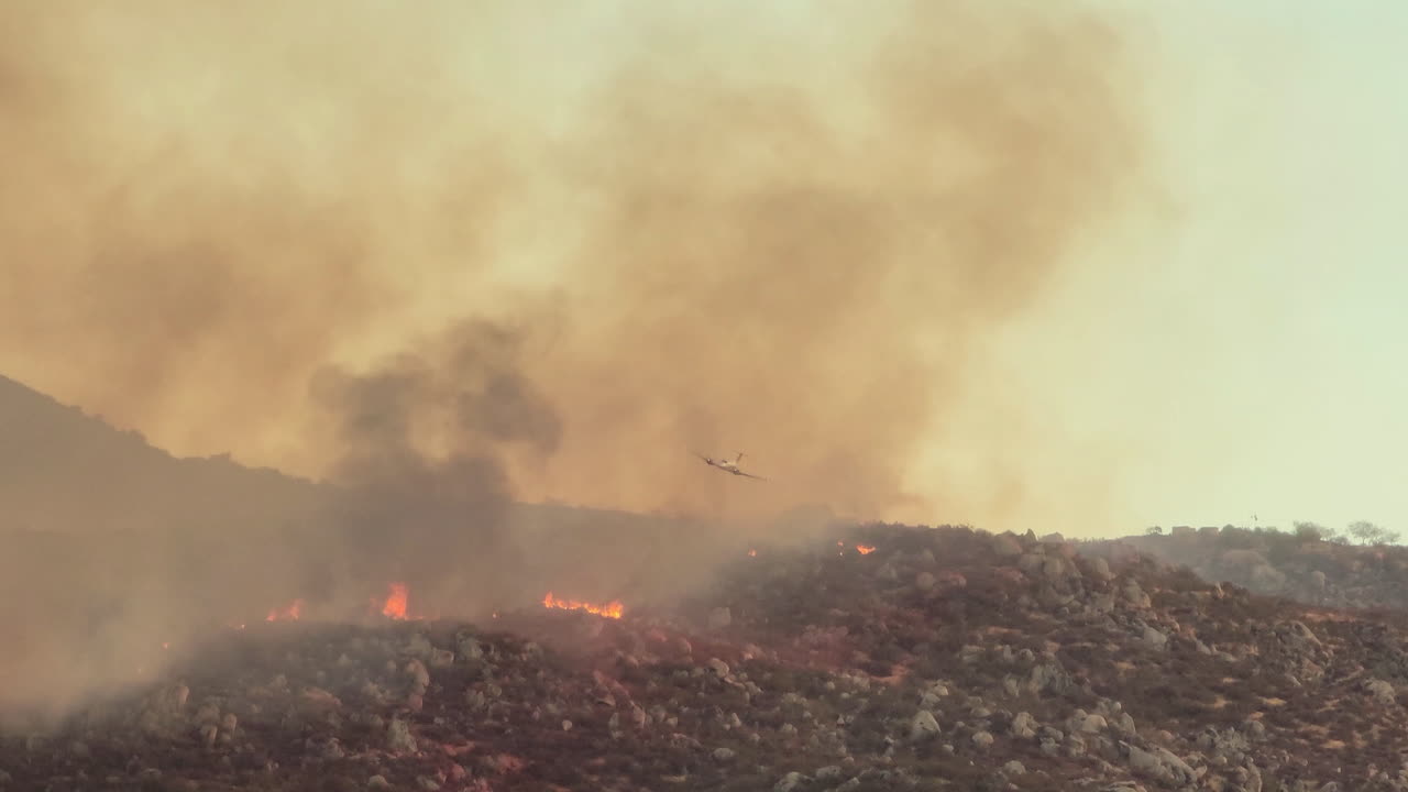 avión de extinción de incendios extinguiendo el fuego arrojando agua química en un terreno accidentado en california