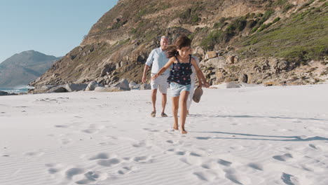 Großeltern-Mit-Enkelin-Spazieren-Im-Sommerurlaub-Am-Sandstrand-Entlang