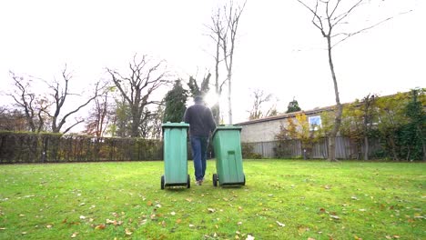 caucasian male worker rolling two trash bins on wheels, slow motion