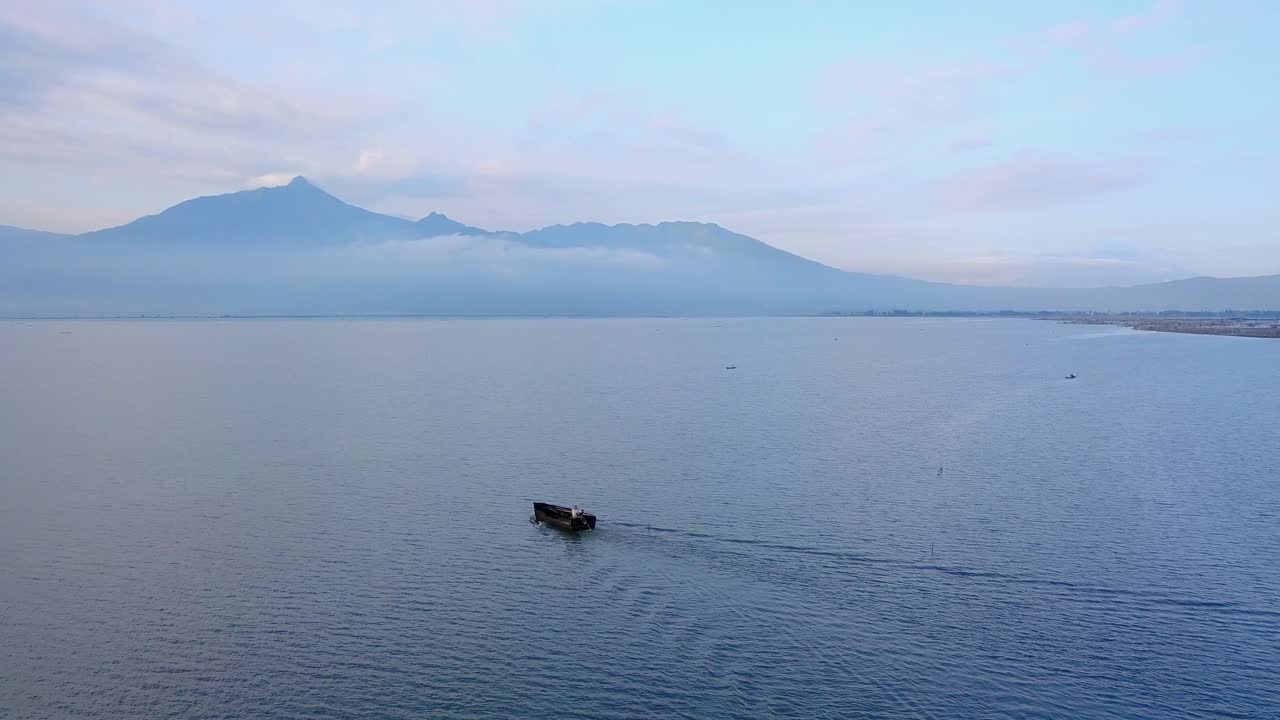 toma de un dron del barco siguiente en el lago con vistas a la montaña en el fondo - lago rawa pening, indonesia