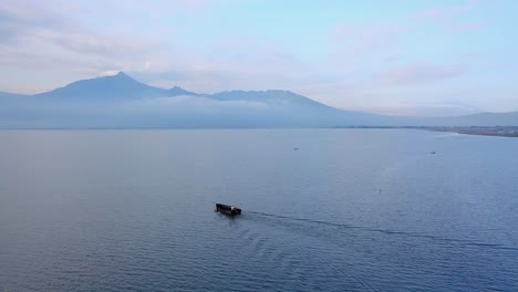 drone shot of following boat on the lake with view of mountain on the background - rawa pening lake, indonesia