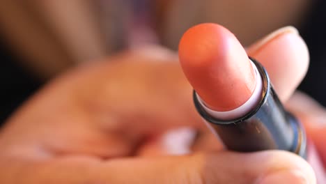 un primer plano de una mujer aplicando lápiz labial de color melocotón