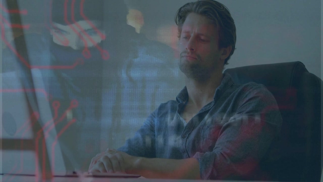 Man pausing typing at desk, causing red circuit lines and binary overlays visualizing tech data