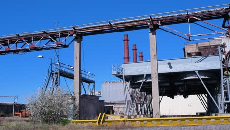 Exterior-view-of-abandoned-Soviet-heavy-metallurgy-melting-factory-Liepajas-Metalurgs-territory,-rust-covered-heat-pipelines,-concrete-poles,-red-brick-chimneys,-sunny-day,-wide-shot