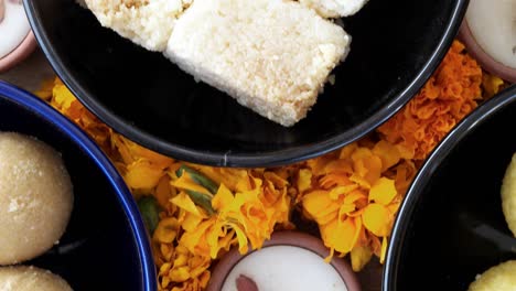 tilt across indian sweets, flowers, diyas on a indian background for hindu festival of lights, dusshera and diwali preparation and celebration ingredients