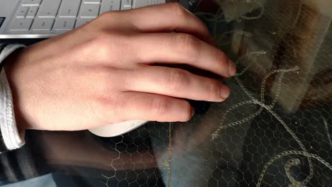 mano femenina usando un mouse de computadora inalámbrico encima de una mesa de vidrio