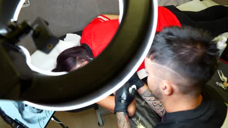 tattooist working on an arm tattoo while female client lies face down