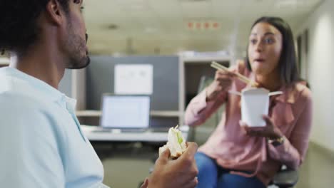 Video-of-happy-diverse-businesswoman-and-businessman-eating-and-talking-in-office