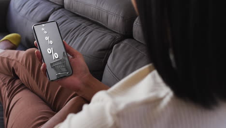 mujer biracial en el sofá usando teléfono inteligente para comprar en línea durante la venta, cámara lenta