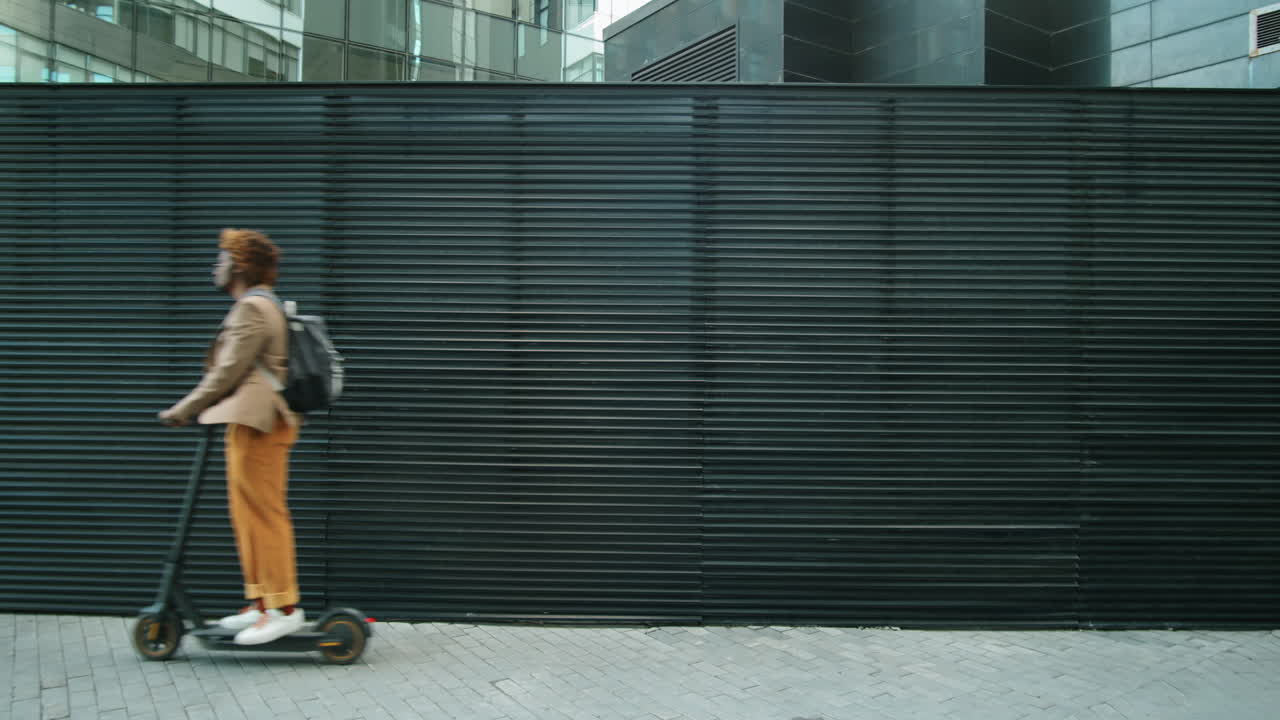 афроамериканский бизнесмен едет на электрическом скутере по улице