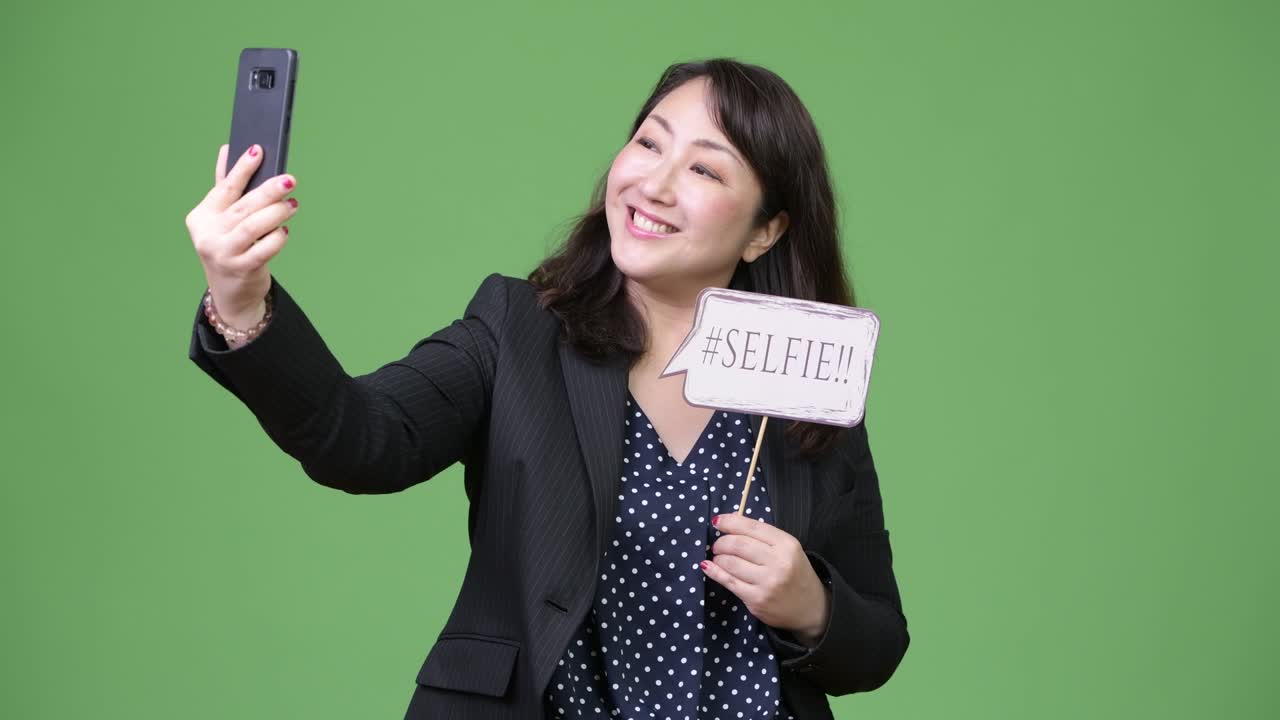Mature beautiful Asian businesswoman taking selfie with paper sign