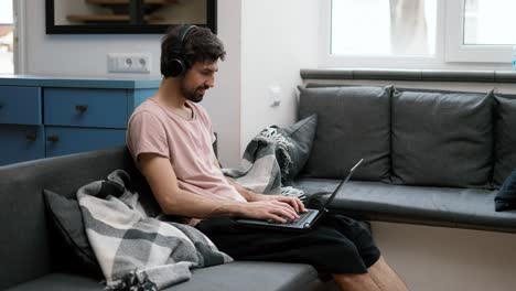 hombre caucásico con auriculares escribiendo en una computadora portátil en casa, cansado terminando el trabajo