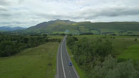 Elevated-view-of-busy-rural-road-A66-heading-towards-mountain-Blencathra-on-cloudy-summer-day