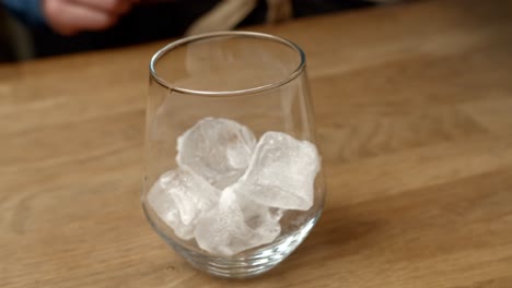 ice cubes fall into glass as bartender makes a drink