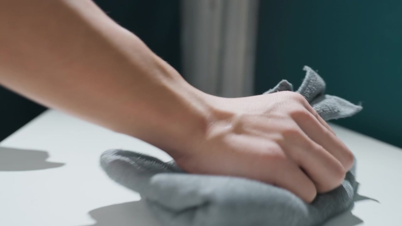 Hands wiping white desk near window, deep clean apartment scene with microfiber cloth, caretakerstyle refresh removes dust and polish surface, natural light highlights streakfree finish and calm