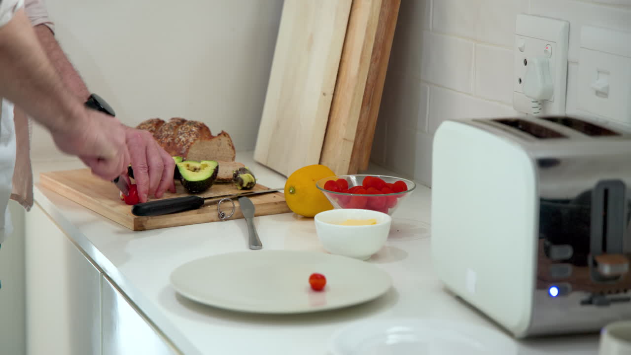 Senior man preparing healthy breakfast with fresh avocado and tomatoes in kitchen, at home