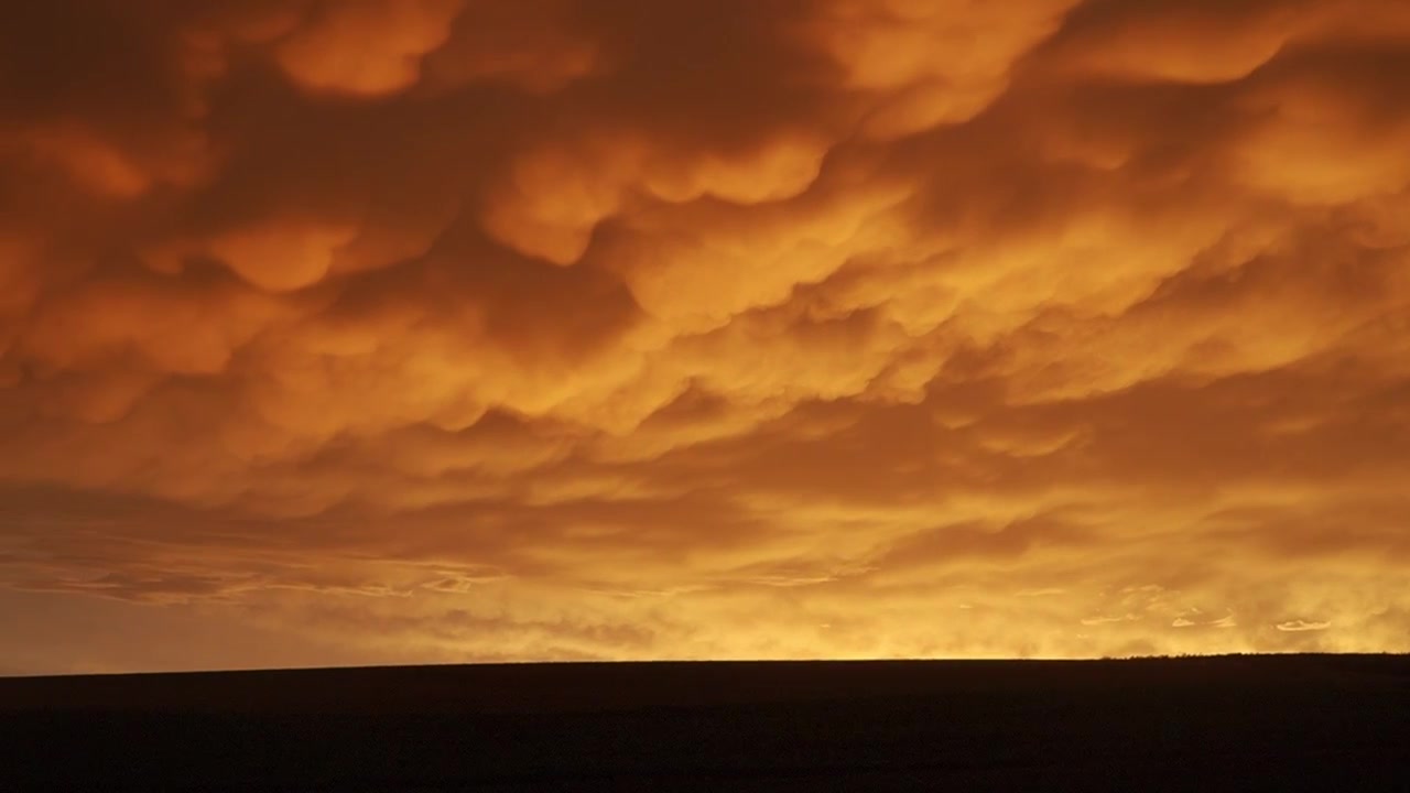 Mammatus-Wolkenformation bei Sonnenuntergang mit leuchtenden gold-orangen Farbtönen. Dramatische atmosphärische Wetterkulisse, die einzigartige himmlische Schönheit während der goldenen Stunde einfängt.