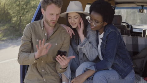 a young male showing his cellphone to two beautiful young girls inside the caravan during a roadtrip