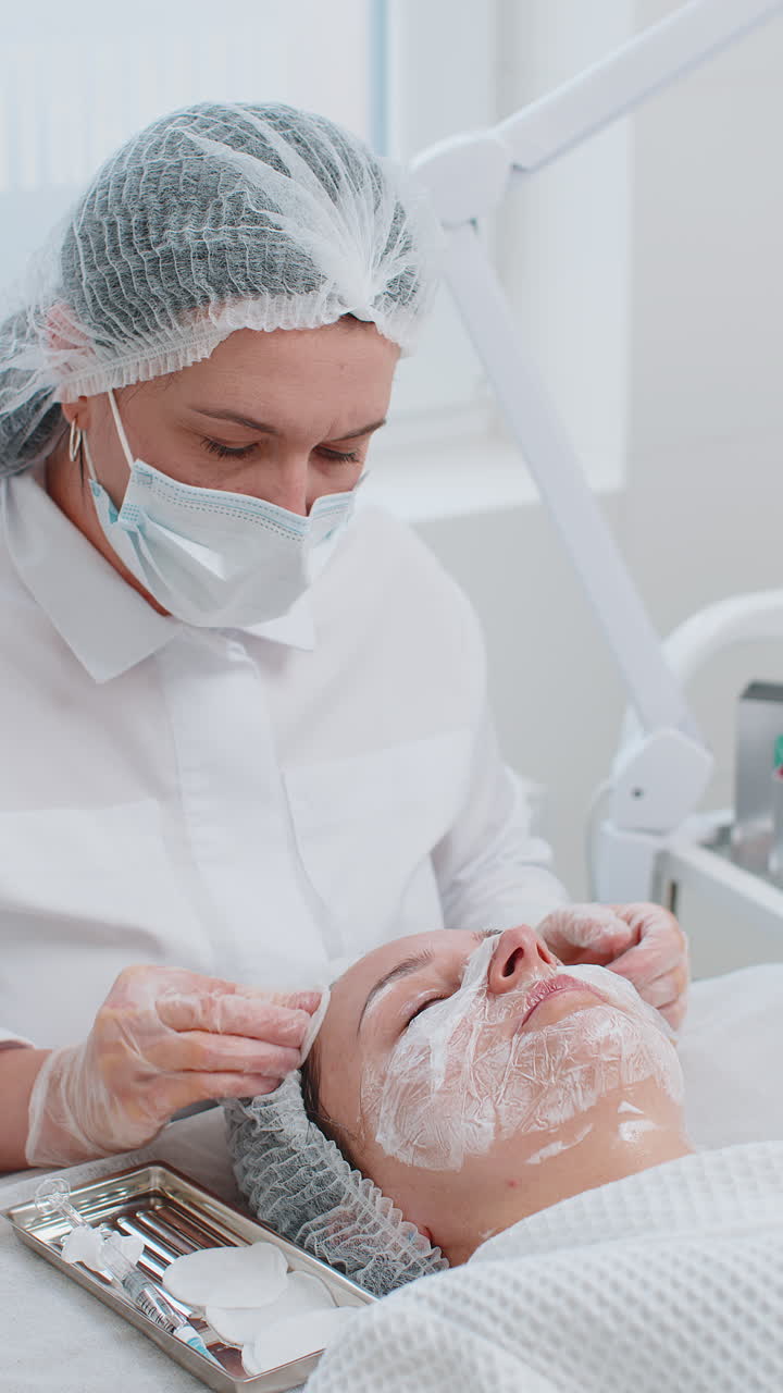 Medico estetico deterge la fronte del viso di una donna con dischetti di cotone durante una procedura di pulizia in una clinica estetica