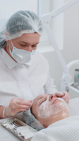 cosmetologist doctor wipes woman face forehead cleaning procedure with cotton wipes in beauty clinic