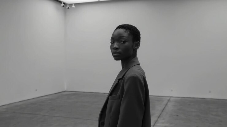 El zoom hace que una mujer con blazer se gire hacia la lente buscando la mirada en una galería con un busto, espacio para texto