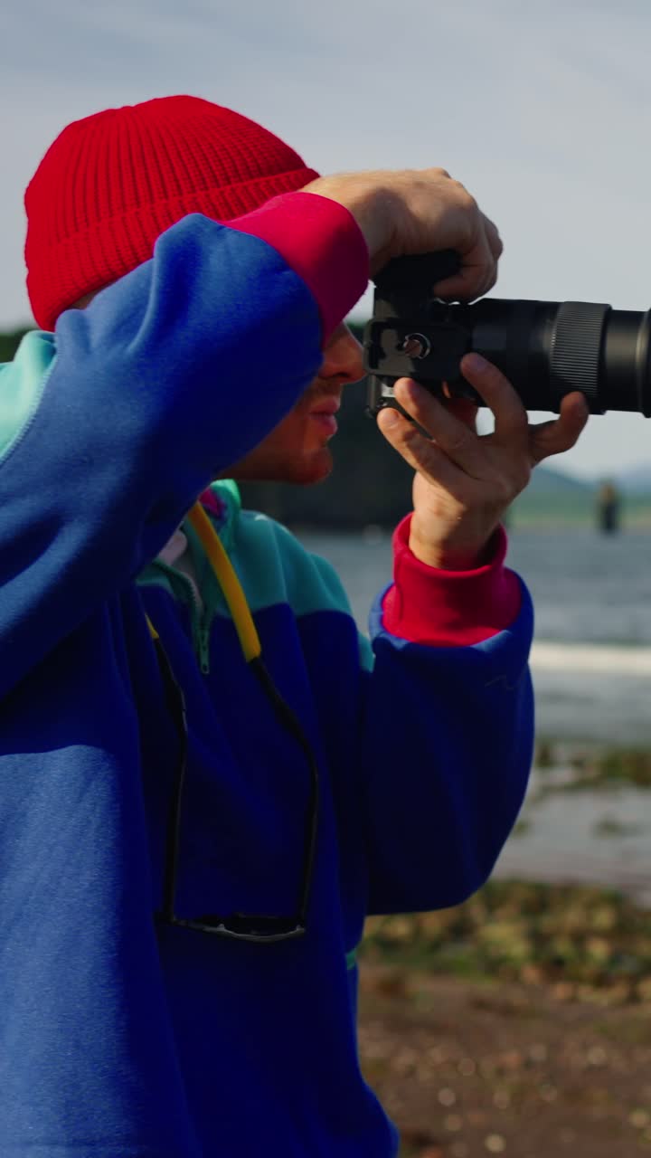 Man in Red Beanie Taking Photos by the Sea