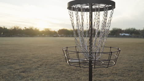 Disc-Golf-Putter-Goes-into-Disc-Golf-Basket-in-open-field-during-the-Late-Evening-Hours-of-the-Day