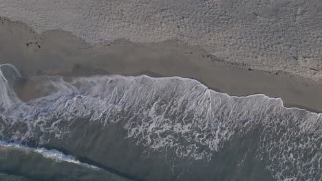 Foamy-ocean-waves-hitting-sandy-beach,-aerial-top-down-shot
