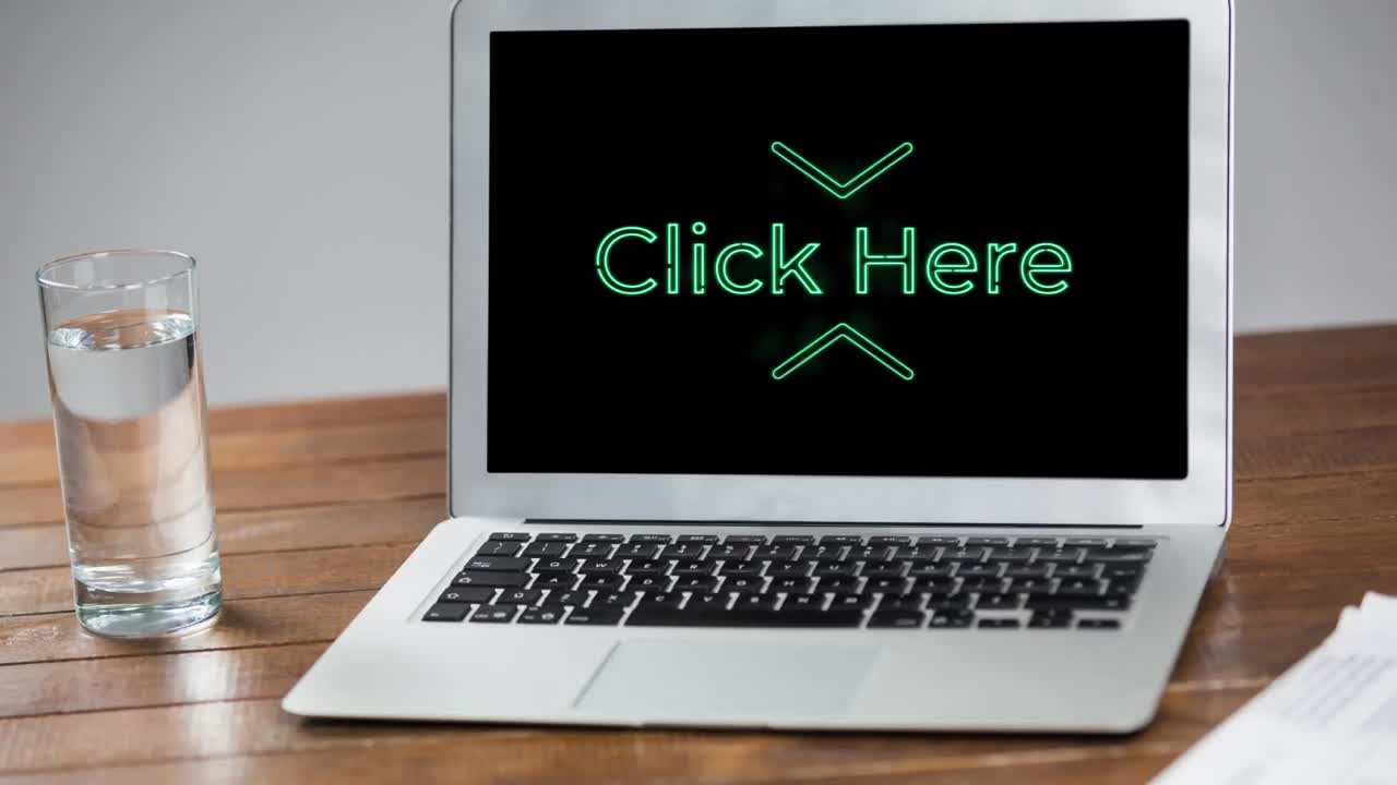 Animation of words Click Here flickering on screen of laptop computer with glass of water