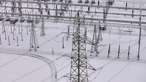 high voltage power pylon with snowy transformation station in the background, drone truck pan